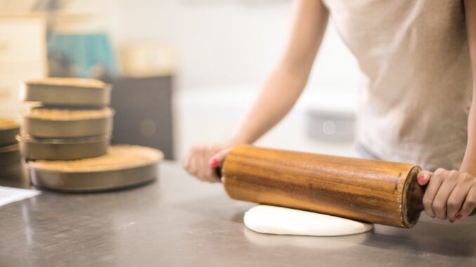 person in white t shirt rolling a pin in dough