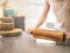 person in white t shirt rolling a pin in dough