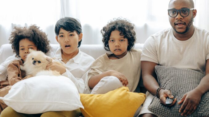 interested multiracial family watching tv on sofa together with dog