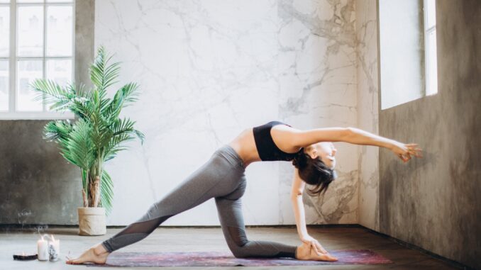 woman in gray leggings and black sports bra doing yoga on yoga mat (wellness trends)