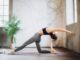 woman in gray leggings and black sports bra doing yoga on yoga mat (wellness trends)