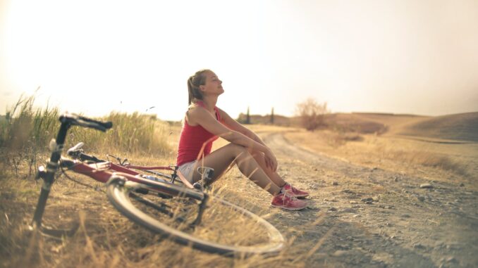 Data reveals that retiring early and paying off the mortgage is at the top of bucket lists! - sportive woman with bicycle resting on countryside road in sunlight