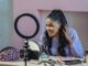 smiling black woman looking at mirror while shooting makeup tutorial