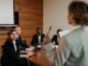 woman in beige business suit holding red and silver ballpen - 'Burnout build-up': 221% surge in demand for burnout support, causing employee exodus HR warning