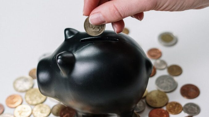 person putting coin in a piggy bank - Experts reveal how to talk to your partner about money