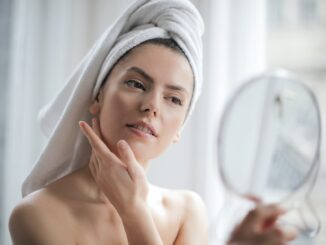 selective focus portrait photo of woman with a towel on head looking in the mirror - Skin Care Routines