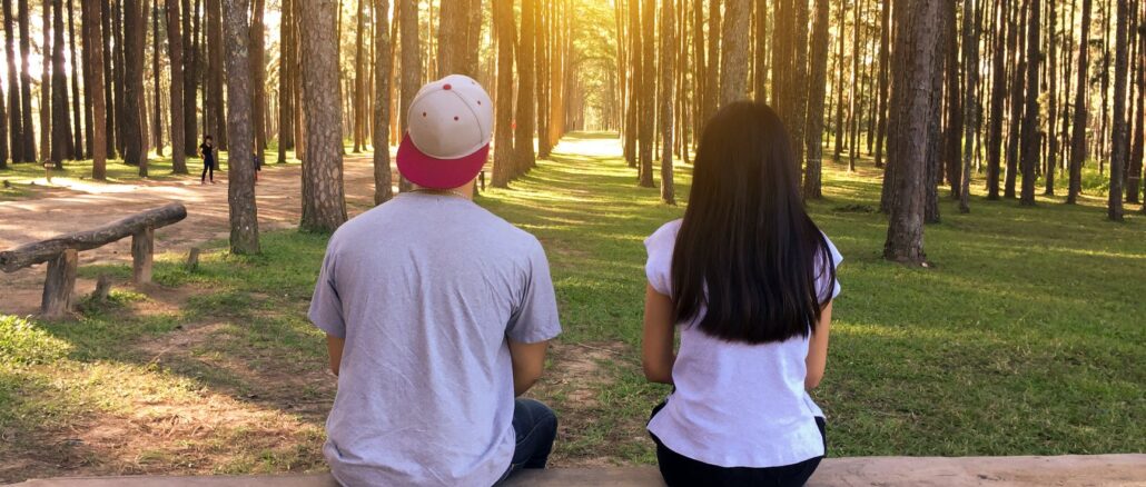 man and woman sitting on bench in woods