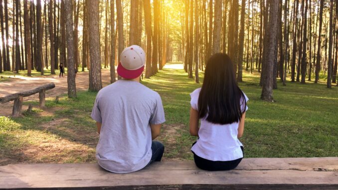 man and woman sitting on bench in woods