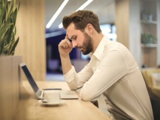 man with hand on temple looking at laptop - revealing their mental health concerns could result in job loss