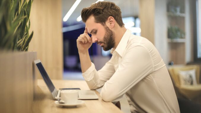 man with hand on temple looking at laptop - revealing their mental health concerns could result in job loss
