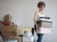 concentrated woman carrying stack of cardboard boxes for relocation